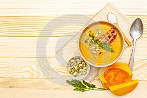 Homemade autumn hot pumpkin cream soup with smocked bacon and seeds. Raw pumpkin, fresh chives, dill, salt in spoon, vintage linen