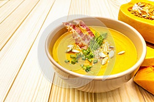 Homemade autumn hot pumpkin cream soup with smocked bacon and seeds. Raw pumpkin, fresh chives, dill, salt in spoon on wooden