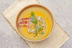 Homemade autumn hot pumpkin cream soup with smocked bacon and seeds. Raw pumpkin, fresh chives, dill, vintage linen cloth on stone
