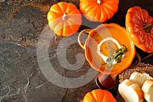 Homemade autumn pumpkin soup in a pumpkin cocette, top view corner border over dark stone background