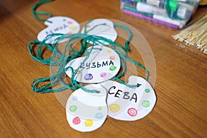 Homemade baby badges on a string. Identification of children at the event. Words: SEVA, KUZMA