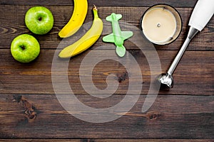 Homemade baby food. Cook puree with apple and banana with immersion blender. Dark wooden background with toy top view