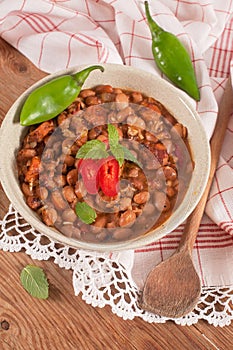 Homemade baked beans in a ceramic plate arranged on rustic wooden table.