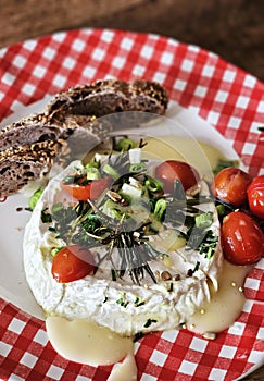 Homemade baked camembert cheese with green onions, rosemary, cherry tomatoes, chives and fresh bread