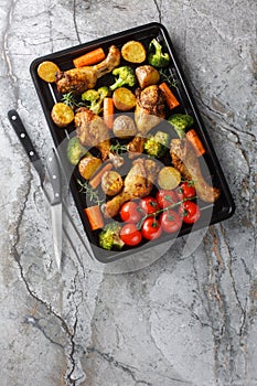 Homemade baked chicken drumsticks with vegetables and rosemary close-up on a baking sheet. Vertical top view