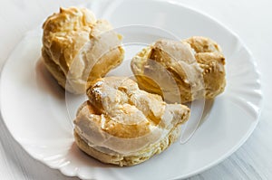 Homemade baked cream puffs on the white plate on light wooden ta