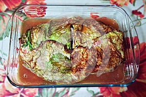Homemade baked huge meat roll in Savoy cabbage green blanch leaves, in glass baking tray with its meat juice. cut out piece from photo