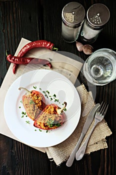 Homemade baked stuffed peppers filled with red lentils with chilly peppers on a white plate, rustic wooden background