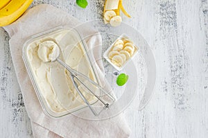 Homemade banana ice cream in a glass container with a spoon for ice cream on a wooden background. Healthy dessert.