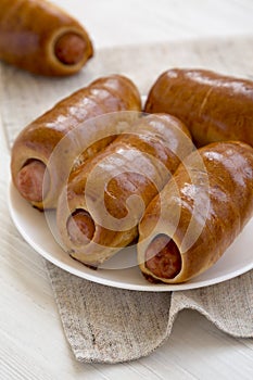 Homemade beef sausage kolache on a white plate on a black background, side view. Close-up