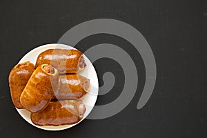 Homemade beef sausage kolache on a white plate on a black background, top view. Flat lay, overhead, from above, overhead. Copy