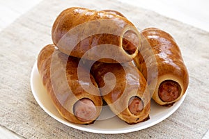 Homemade beef sausage kolache on a white plate on a white wooden background, side view. Close-up