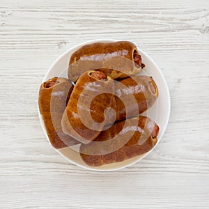 Homemade beef sausage kolache on a white plate on a white wooden background, top view. Flat lay, overhead, from above. Close-up