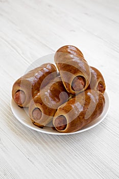 Homemade beef sausage kolache on a white plate on a white wooden surface, low angle view. Close-up