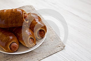 Homemade beef sausage kolache on a white plate on a white wooden surface, side view. Copy space