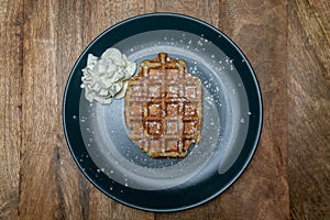 Homemade Belgian waffle on a plate. With powder sugar on it and whipped cream on the side. Top view