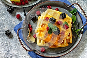 Homemade Belgian waffles with berries and honey on a stone countertop