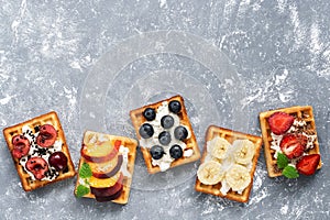 Homemade Belgian waffles with a variety of fruits on a gray background. Top view, copy space.