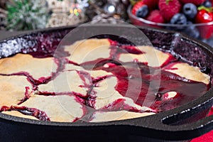 Homemade berry cobbler in cast iron skillet, Christmas decoration on background, horizontal, closeup