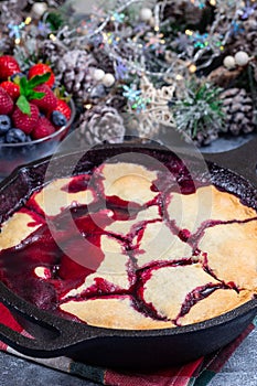 Homemade berry cobbler in cast iron skillet, Christmas decoration on background, vertical