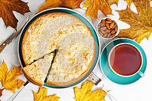 Homemade berry pie decorated with almond petals and cup of tea on white wooden table.