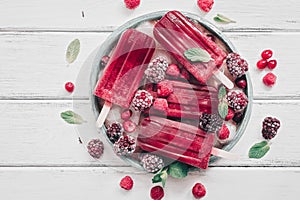 Homemade berry popsicles decorated berries and mint leaves on a white rustic wooden plank. Overhead view,flat lay