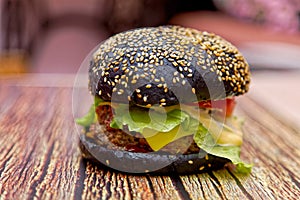 Homemade black burger with meat cutlet, tomatoes, salad and cheese on a wooden table. Shallow depth of field