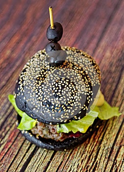 Homemade black burger with meat cutlet, tomatoes, salad and cheese on a wooden table. Shallow depth of field