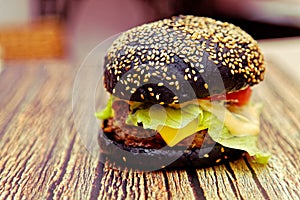 Homemade black burger with meat cutlet, tomatoes, salad and cheese on a wooden table. Shallow depth of field