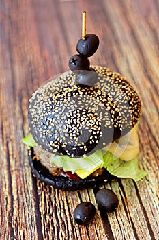 Homemade black burger with meat cutlet, tomatoes, salad and cheese on a wooden table. Shallow depth of field