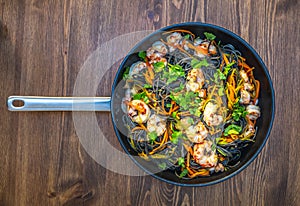 Homemade black spaghetti with cuttlefish ink, with shrimp, dill and carrots. in a pan on a wooden table. healthy home