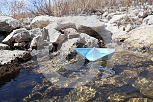 A homemade blue paper boat was launched into a stream with stones