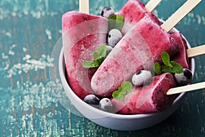 Homemade blueberry ice cream or popsicles decorated green mint leaves on teal rustic table, frozen fruit juice