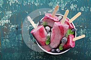 Homemade blueberry ice cream or popsicles decorated green mint leaves on teal rustic table, frozen fruit juice