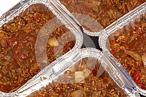 Homemade bolognese sauce filled in individual foil trays ready for freezing.