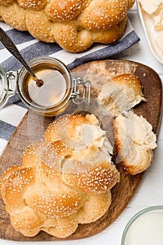 Homemade braided bread with sesame seeds, butter and honey on white wooden table, flat lay. Traditional challah