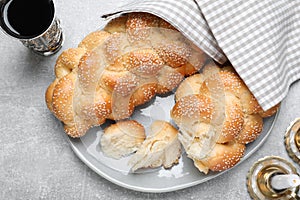 Homemade braided bread with sesame seeds and goblet on grey table, flat lay. Traditional Shabbat challah