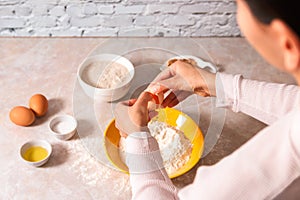 Homemade bread baking. closeup woman hands adding egg in flour, dough preparation in bright kitchen with marble countertop