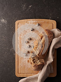 Homemade bread with black olives broken on a wooden chopping board and black olives, flour and decorative towel