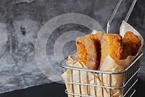 Homemade breaded fish fingers in a wire basket with greaseproof paper. photo