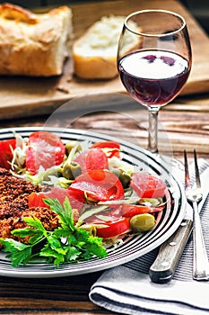 Homemade Breaded German Weiner Schnitzel and fresh vegetable spring salad with tomato, green olives, cabbage and parsley