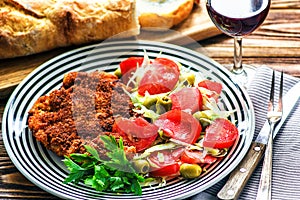 Homemade Breaded German Weiner Schnitzel and fresh vegetable spring salad with tomato, green olives, cabbage and parsley