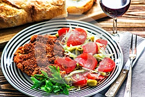 Homemade Breaded German Weiner Schnitzel and fresh vegetable spring salad with tomato, green olives, cabbage and parsley photo