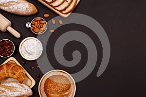 Homemade breads or bun, croissant and bakery ingredients, flour, almond nuts, hazelnuts, eggs on dark background, Bakery