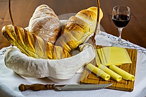 Homemade breads. different types of home made breads in basket with cutting board with cheese and glass of wine beside on white ta