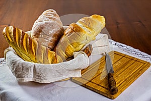 Homemade breads. different types of home-made breads in basket with wooden cutting board and knife beside on white tablecloth on w