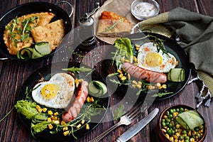 Homemade breakfast concept. Appetizing scrambled eggs, sausages, vegetables and herbs on dark plates on a rustic background