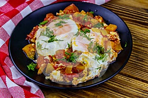 Homemade breakfast shakshuka - fried eggs, onion, bell pepper, tomatoes and dill on rustic wooden table. Jewish cuisine