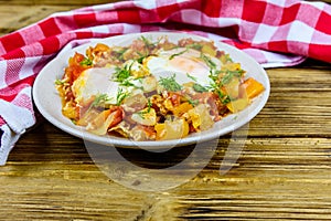 Homemade breakfast shakshuka with fried eggs, onion, bell pepper, tomatoes and dill on a wooden table. Jewish cuisine