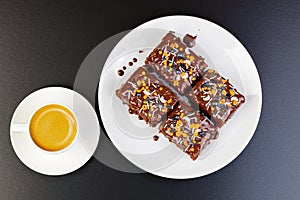 Homemade brownie and cups of coffee espresso on dark table.